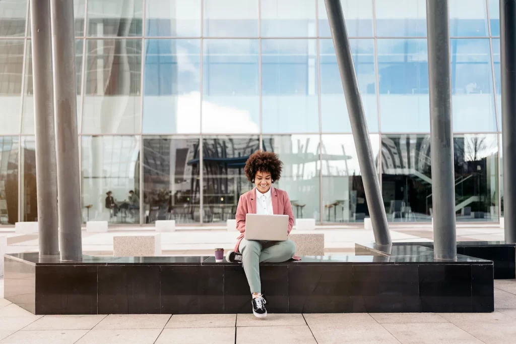 Mujer sentada al aire libre, con un computador, representando búsquedas en google